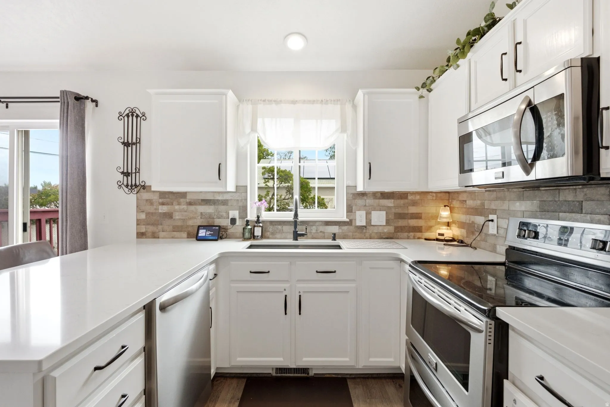 White cabinetry with dark hardware, stone tile backsplash, stainless steel appliances, and white countertops