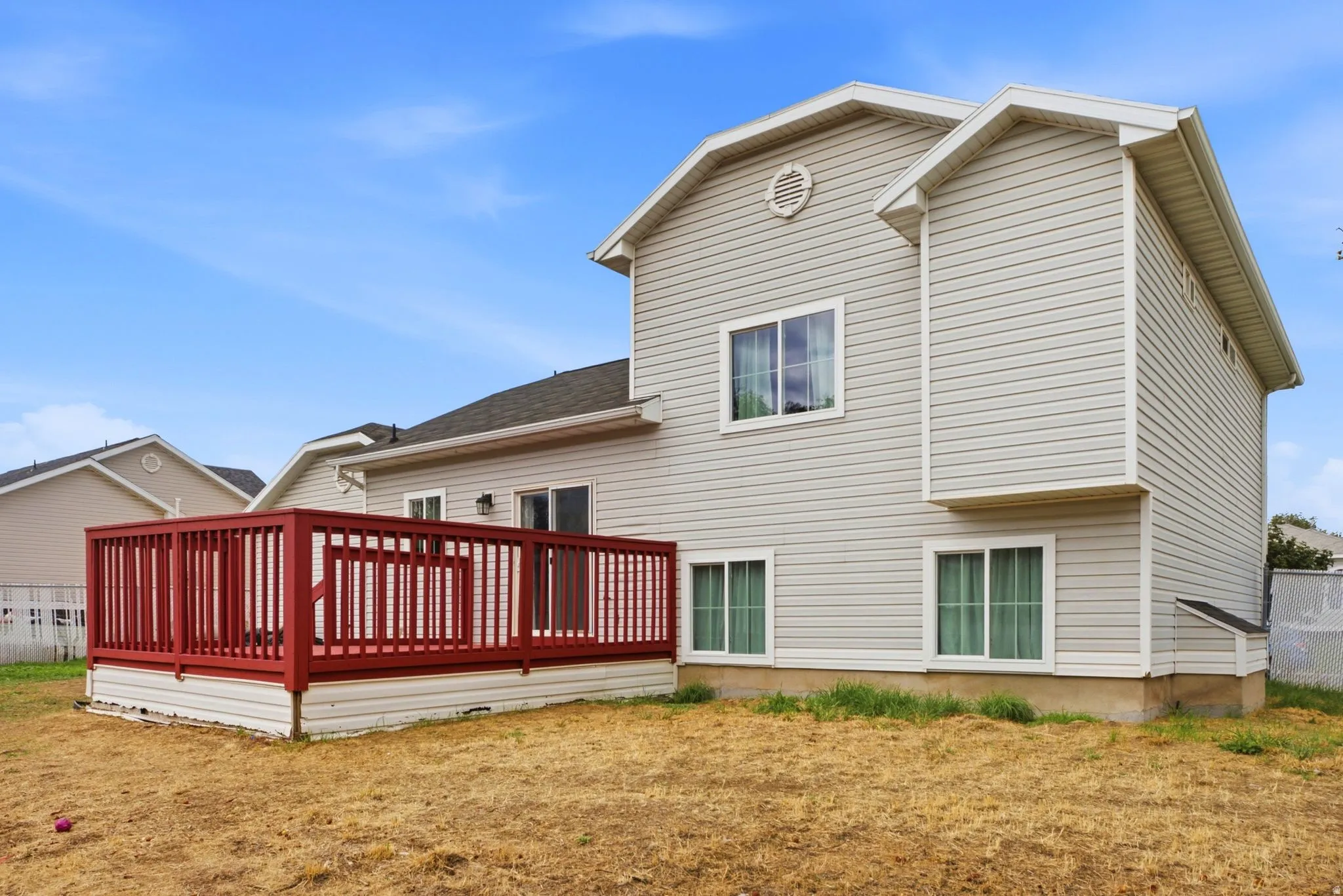 Exterior featuring light-colored siding, multiple windows, and a prominent red-stained wood deck