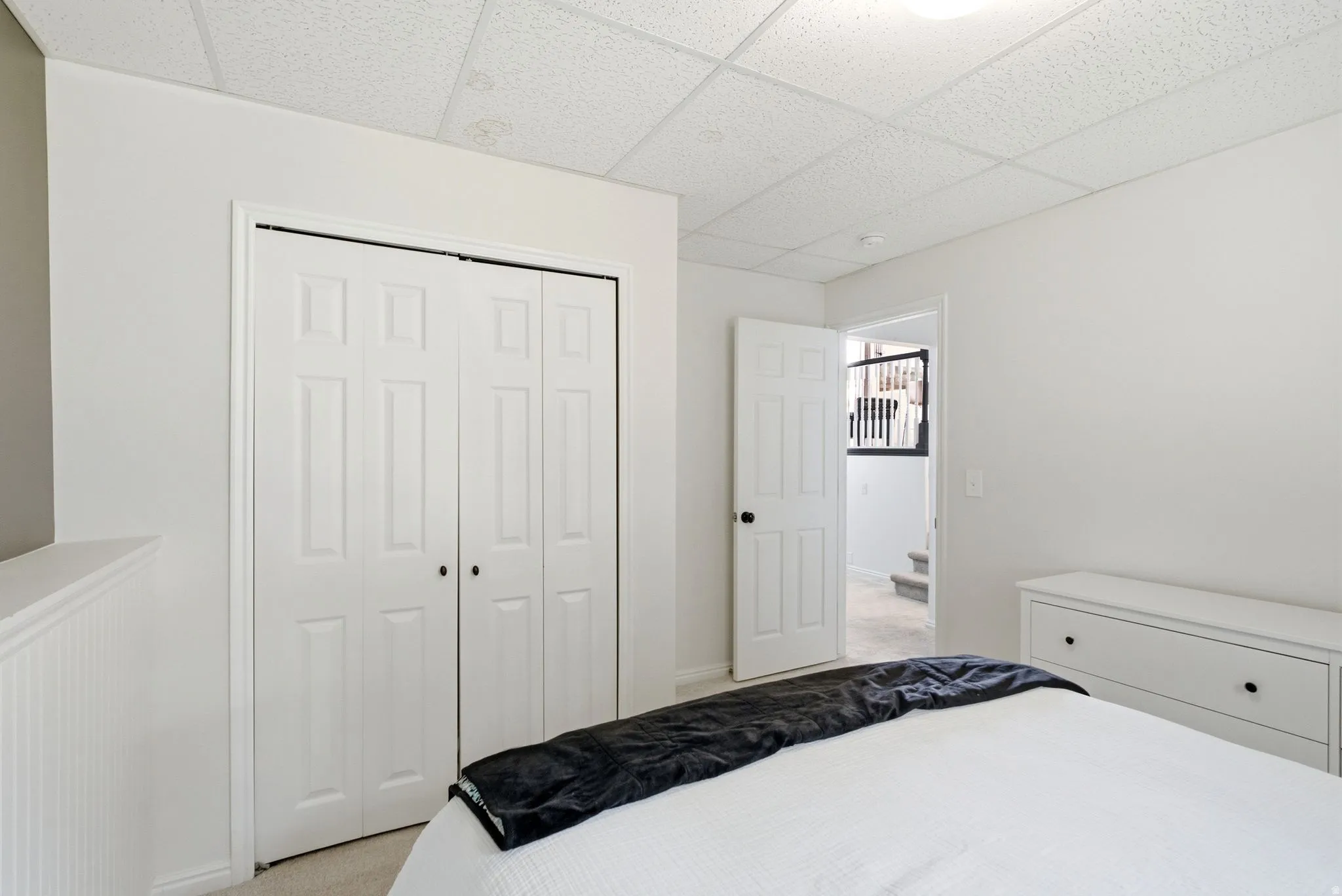 Bright bedroom with dual closet storage featuring white six-panel doors, white painted wood-finish dresser with drawer storage, and crisp white bedding