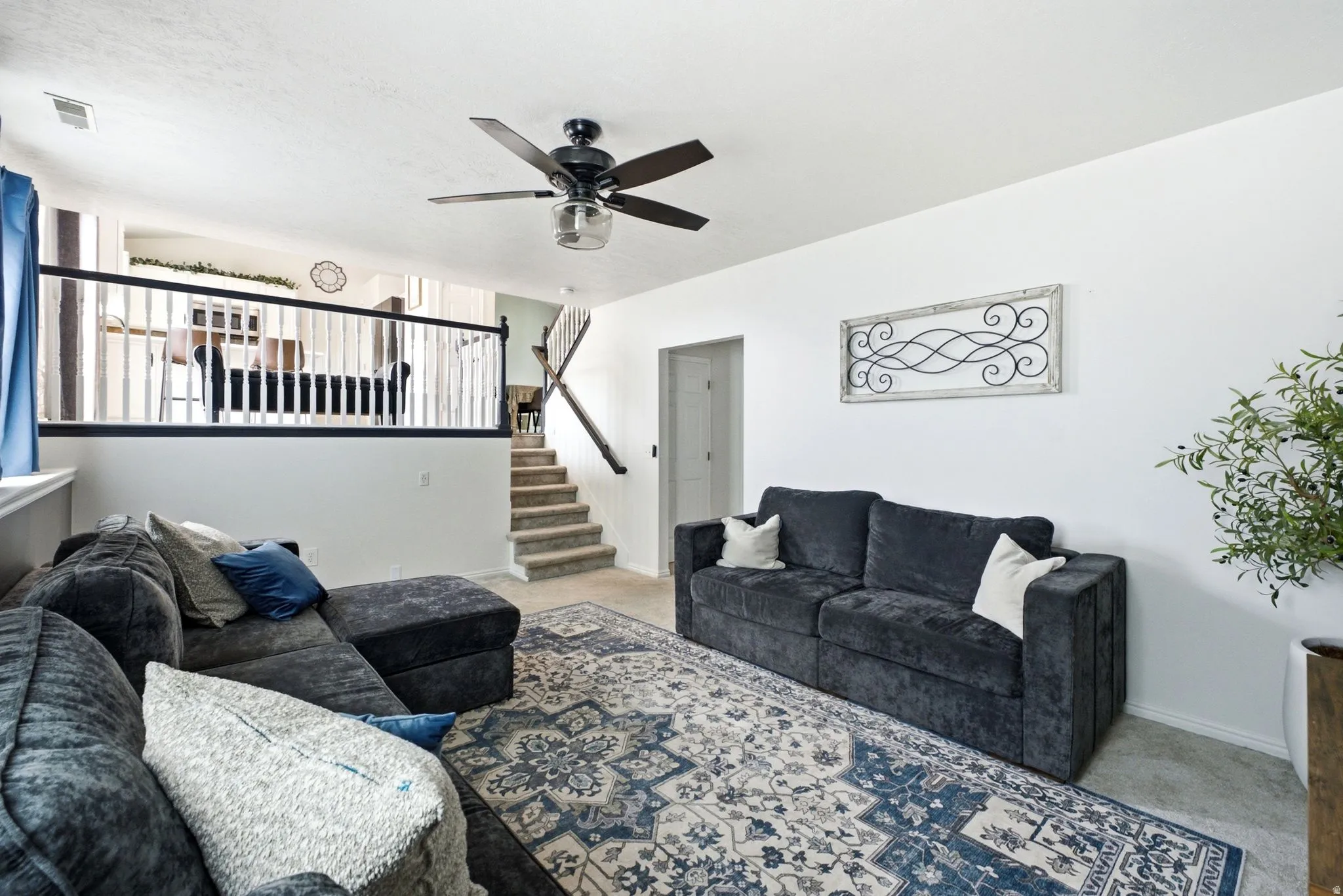 Open-concept living area featuring a ceiling fan, a staircase with a wood handrail, and a half-wall with white balusters