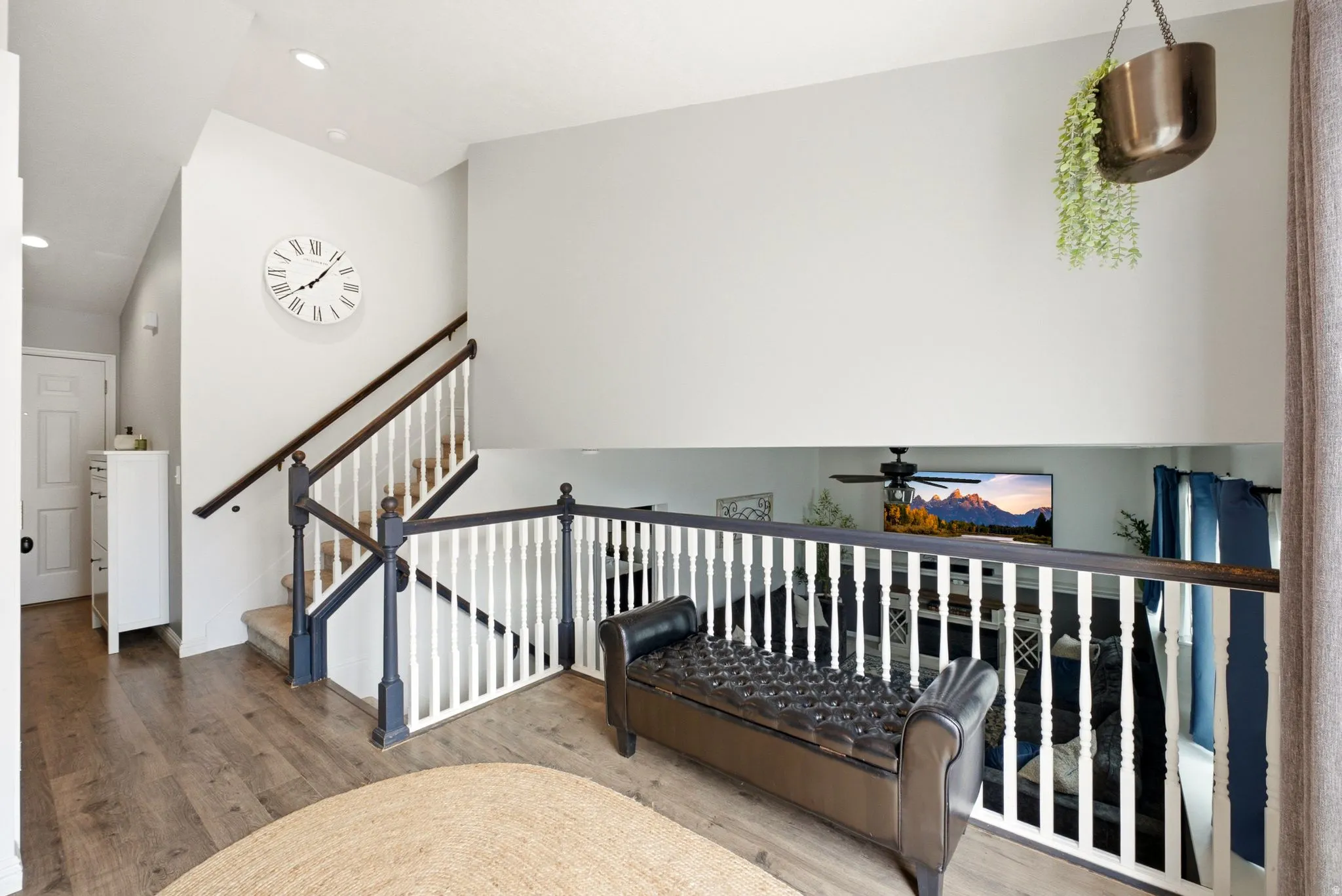 Upper-level landing featuring wood-finish flooring, white railing with dark wood-finish top rail, and recessed lighting