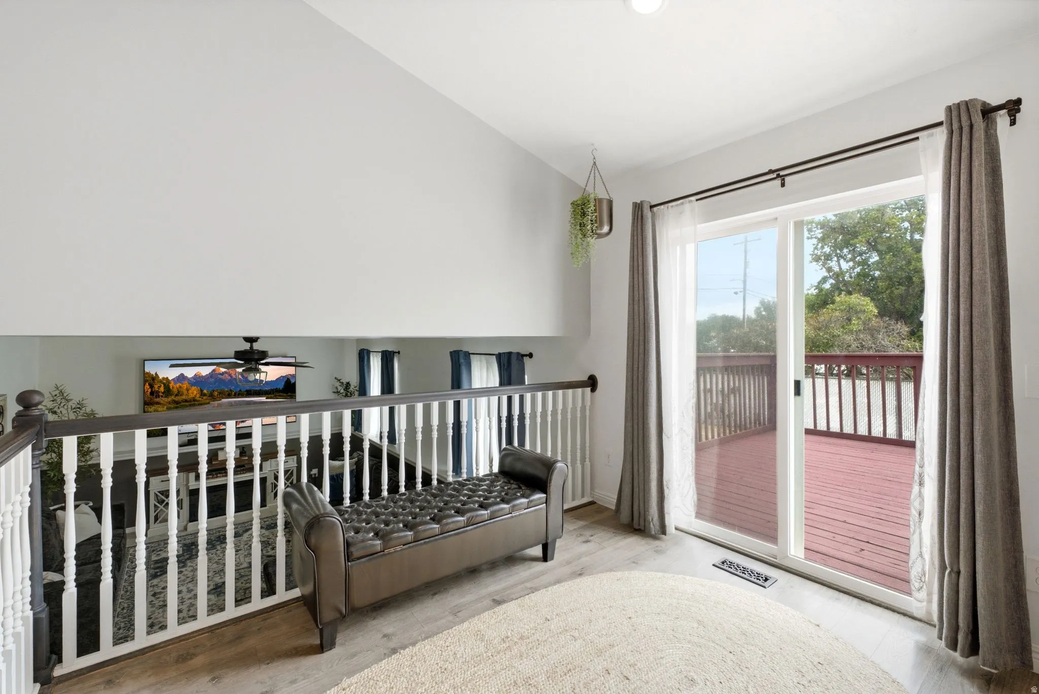 Sliding glass door opening to an exterior deck with white railing, wood-finish flooring, and a white balustrade overlooking a lower level