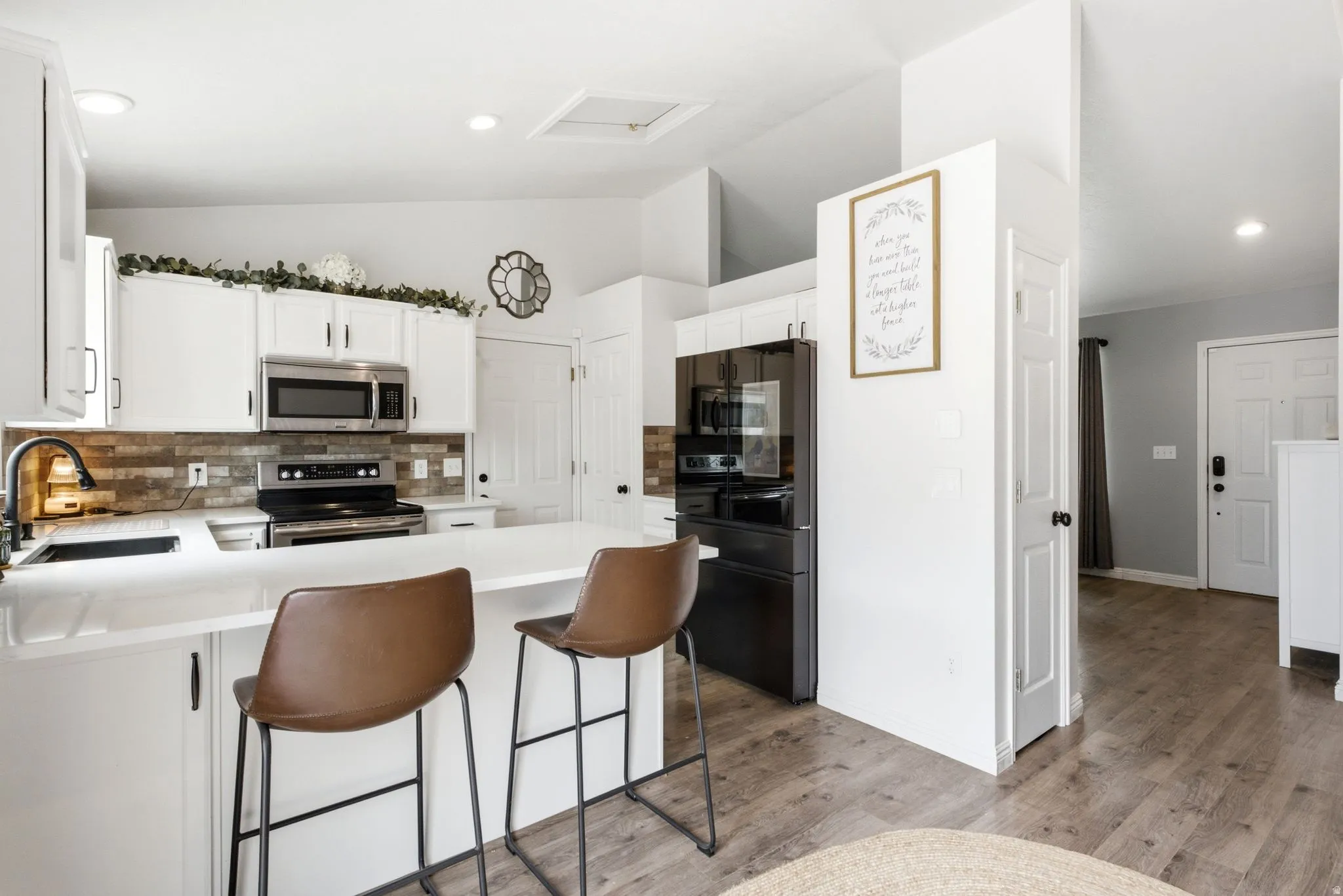White shaker cabinetry, stainless steel appliances, solid surface countertops, wood-finish flooring, and a stone-look backsplash