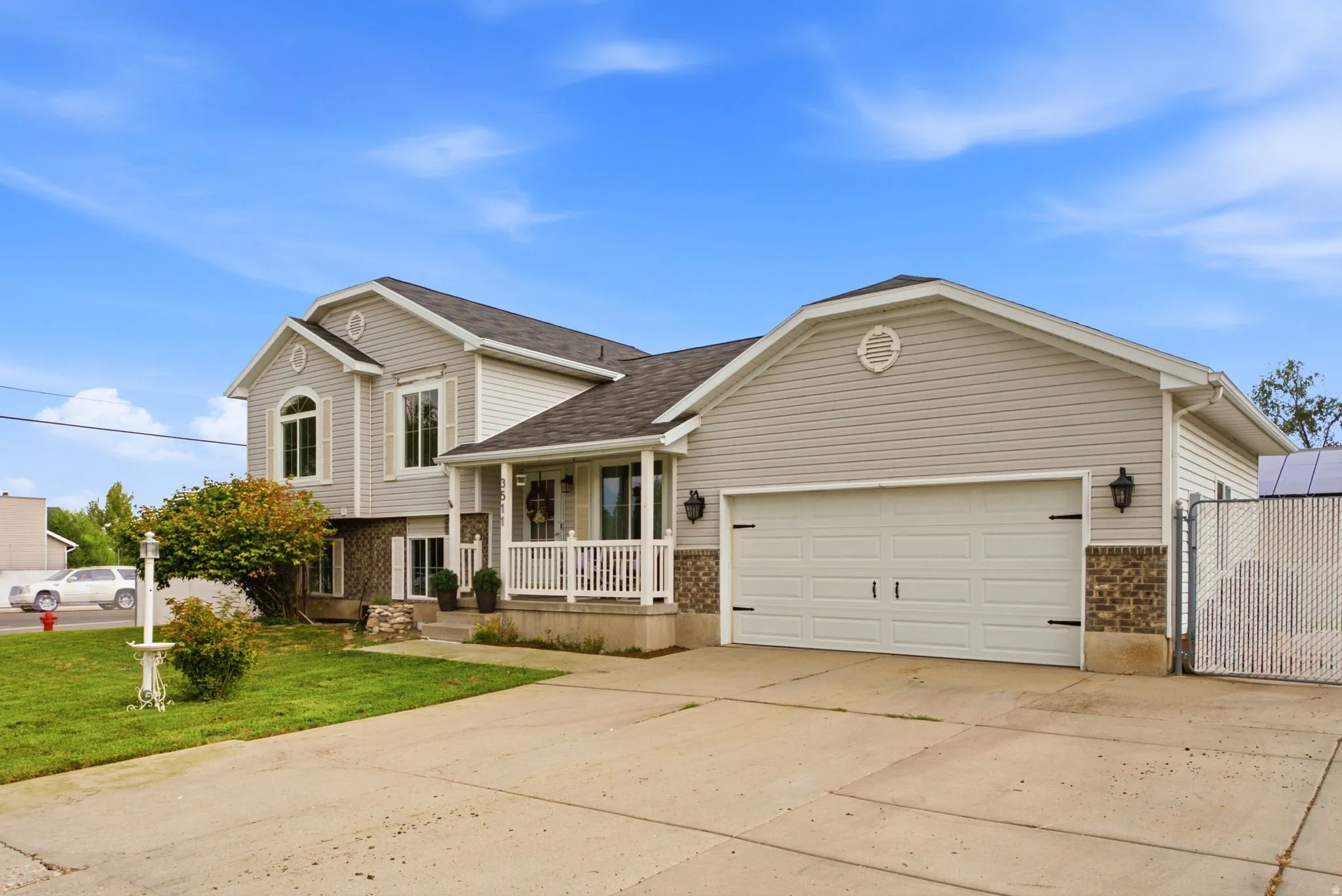 Two-story residence featuring light-colored siding, a covered front porch with white railing, an attached two-car garage, and a concrete driveway