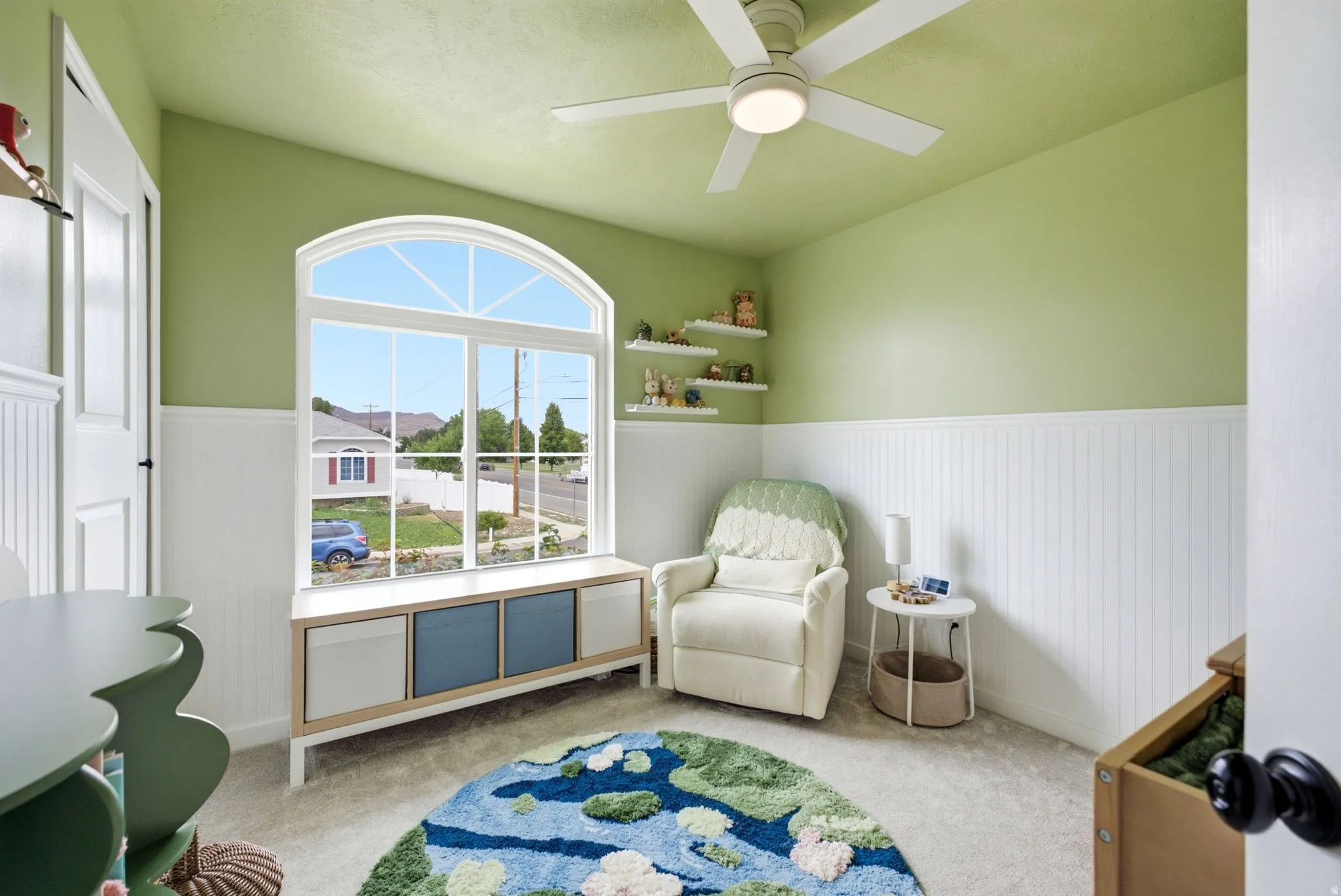 Arched window with a built-in window seat, beadboard wainscoting, and a ceiling fan with integrated lighting