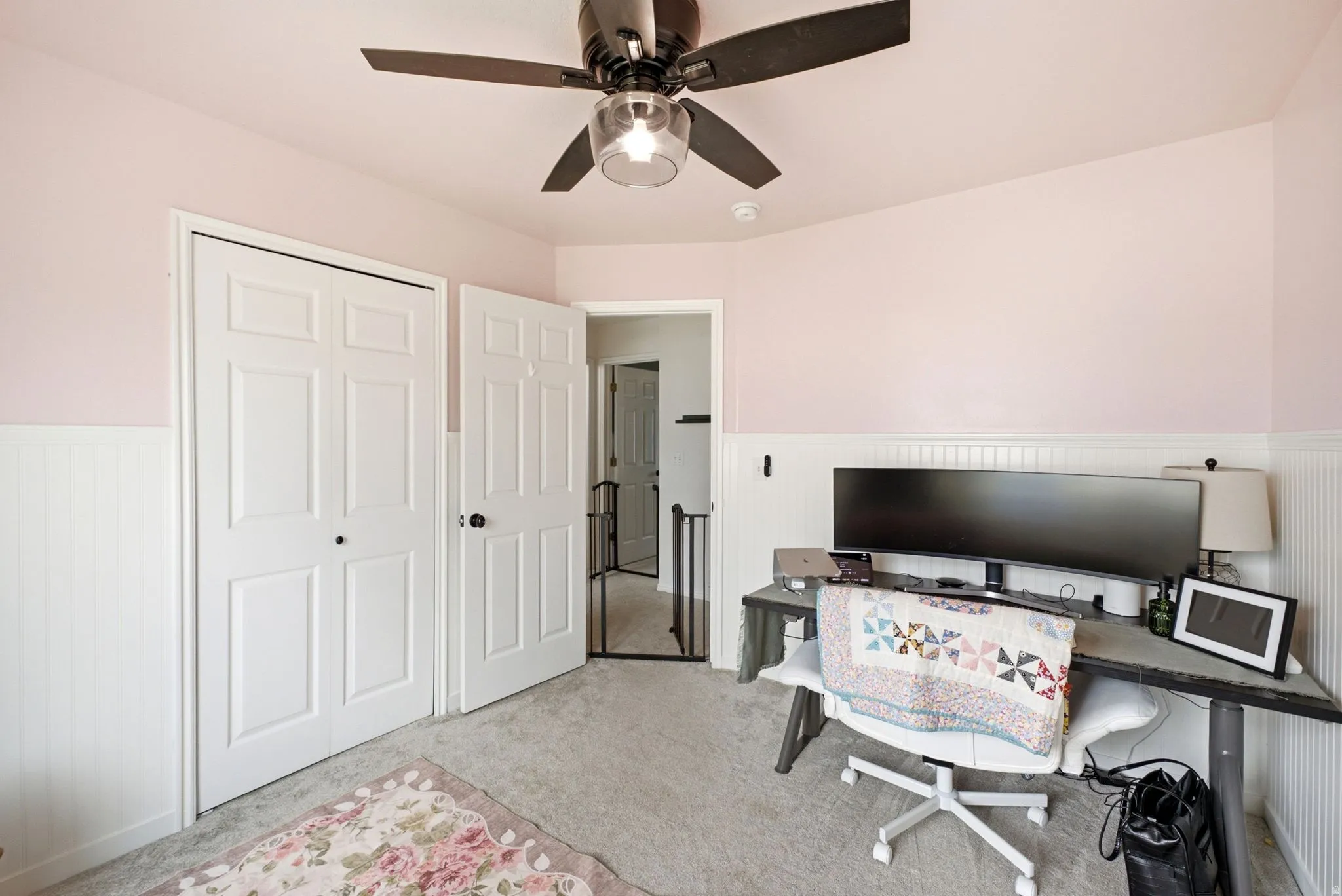Ceiling fan with integrated lighting, wall-to-wall carpeting, beadboard wainscoting, and white paneled doors