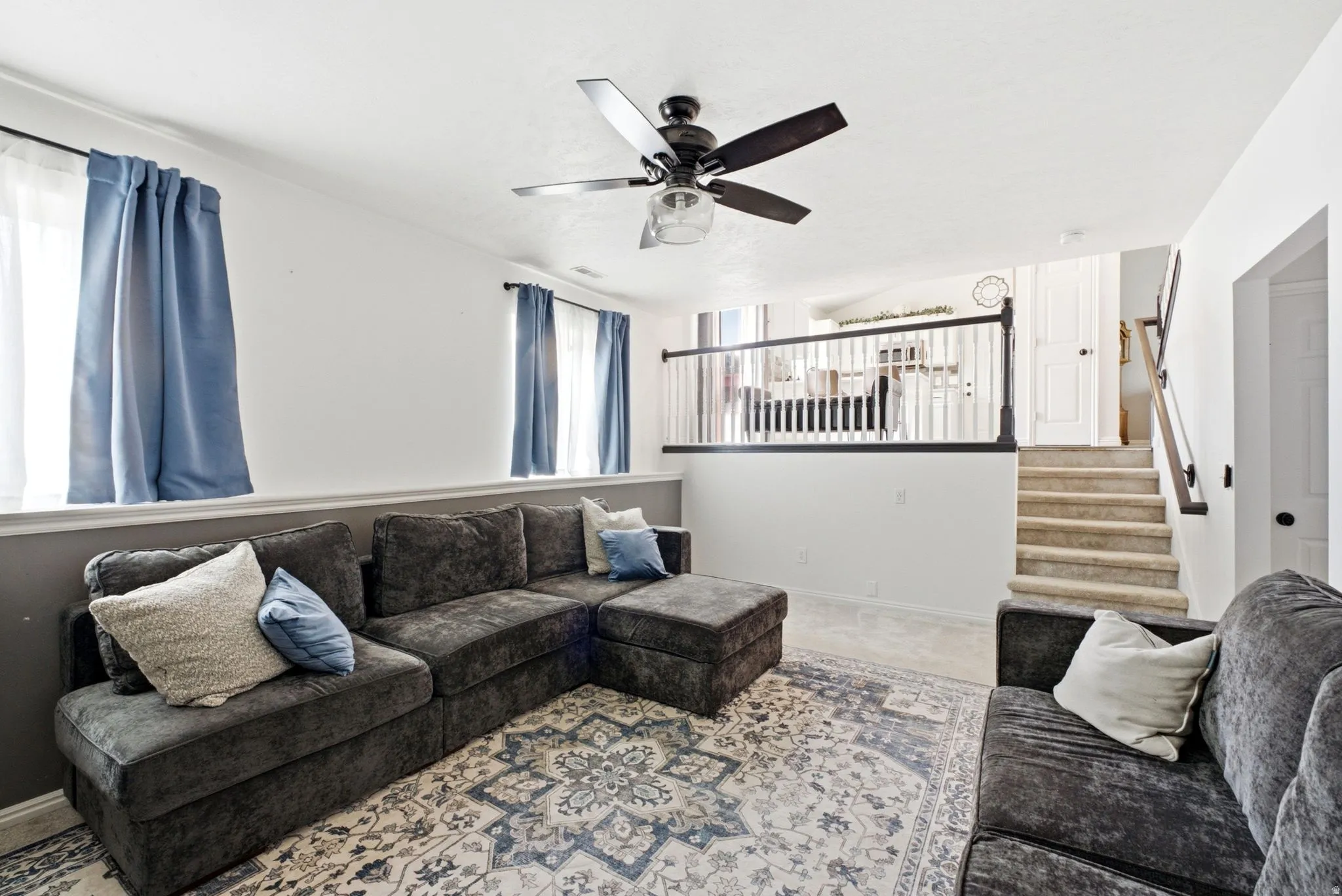 Recessed lighting, wood-finish railing, carpeted staircase, ceiling fan light fixture, and windows with natural light