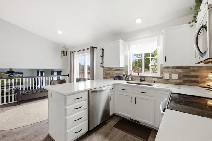 White shaker cabinetry, stainless steel appliances, quartz countertops, tile backsplash, and wood-finish flooring
