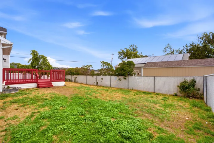 Expansive backyard featuring a red wood-finish deck with railings and steps, and chain-link fencing