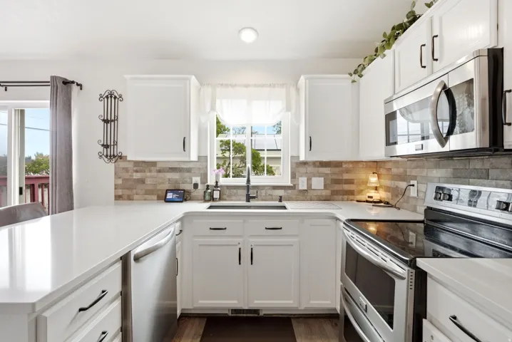 White cabinetry with dark hardware, stone tile backsplash, stainless steel appliances, and white countertops