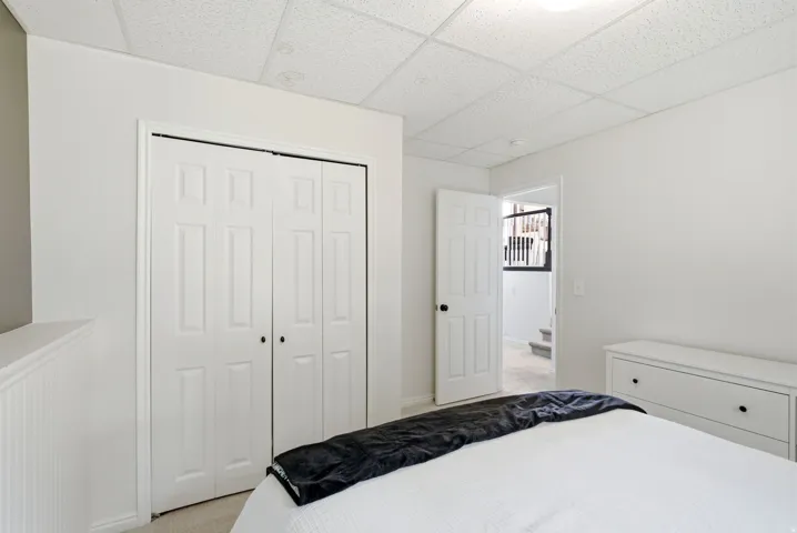 Bright bedroom with dual closet storage featuring white six-panel doors, white painted wood-finish dresser with drawer storage, and crisp white bedding