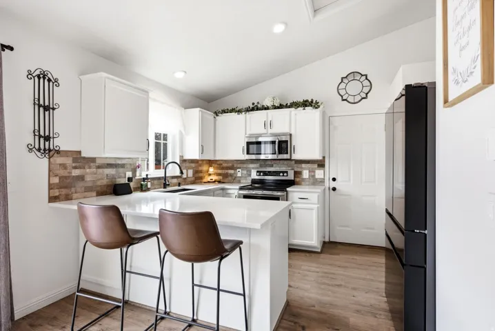 Kitchen featuring a U-shaped counter, white cabinetry, a stone-look backsplash, stainless steel appliances, and wood-finish flooring