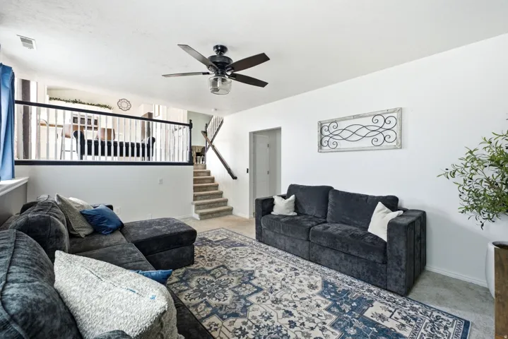 Open-concept living area featuring a ceiling fan, a staircase with a wood handrail, and a half-wall with white balusters