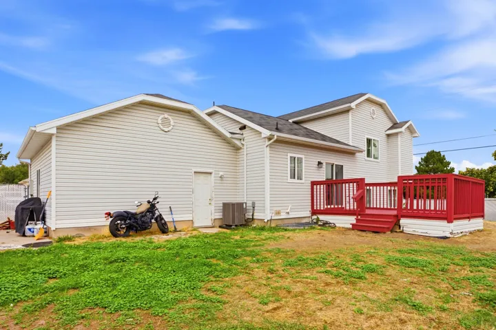 Rear exterior featuring light-colored siding, a red deck with railings, and an air conditioning unit