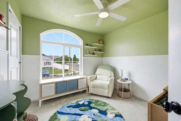 Arched window with a built-in window seat, beadboard wainscoting, and a ceiling fan with integrated lighting