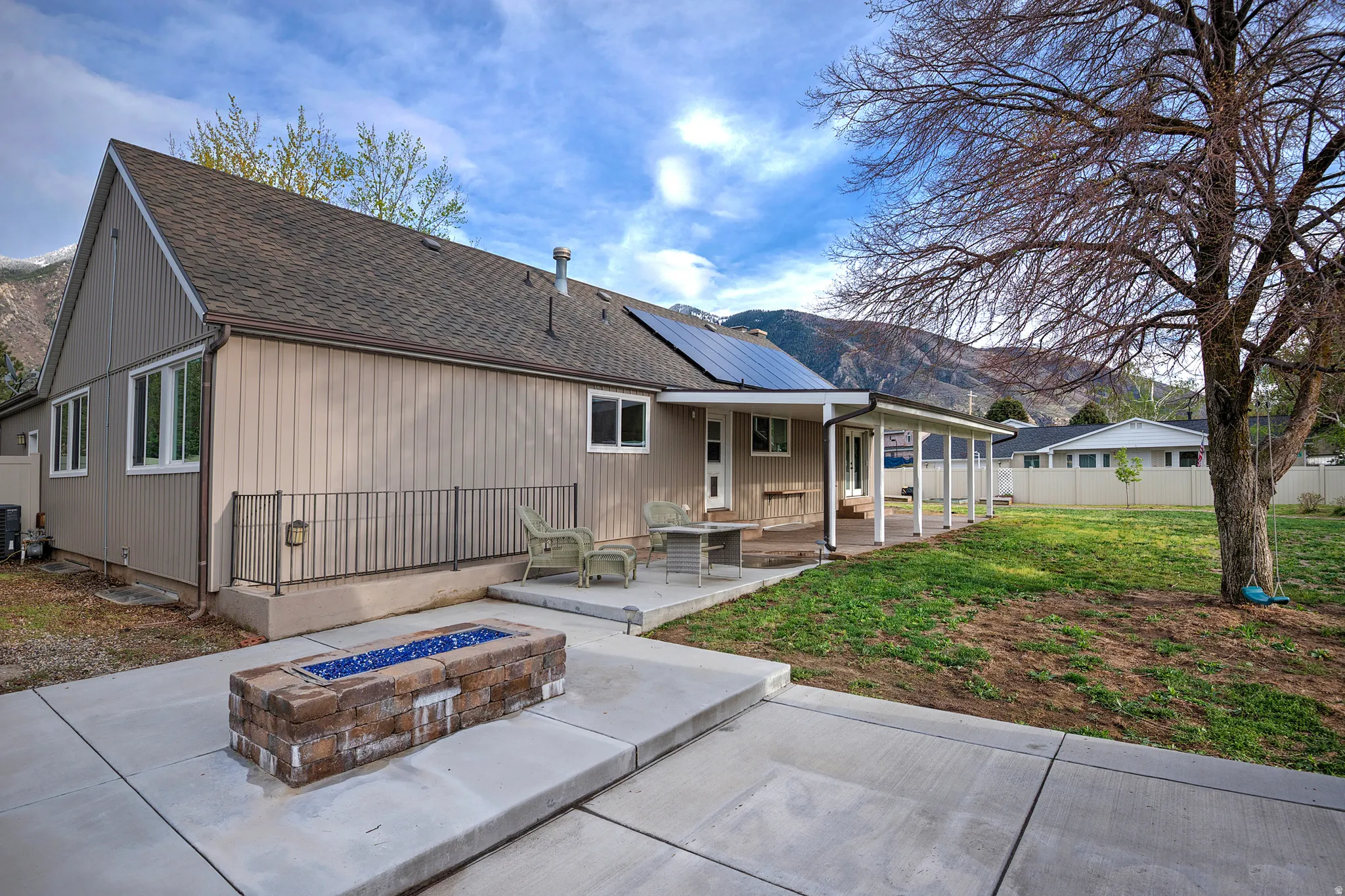 Rear exterior with an extended covered patio, a paver and concrete fire pit, and solar panels on the roof