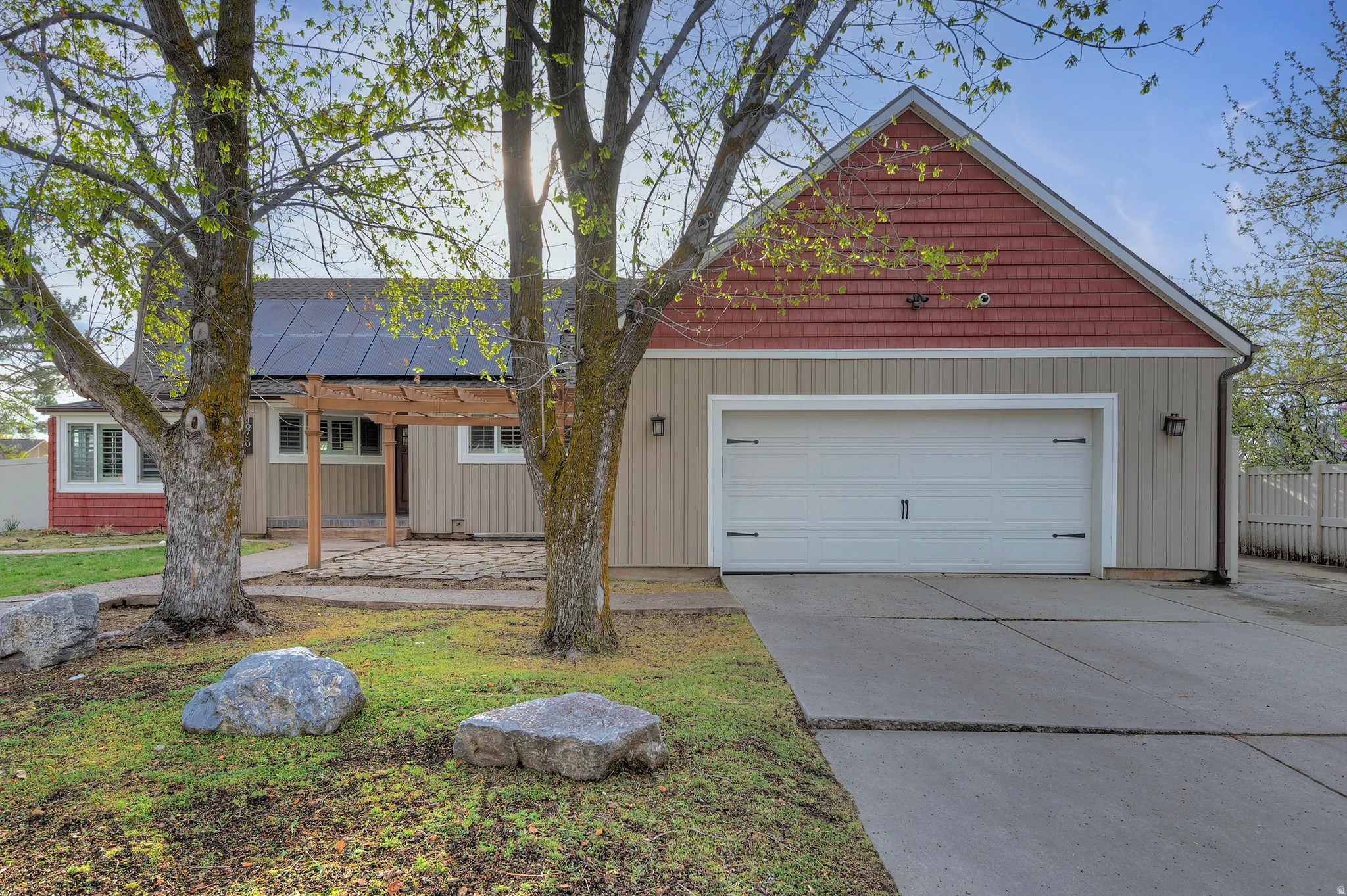 Exterior featuring a two-car garage, solar panels, a wooden pergola, and a concrete driveway