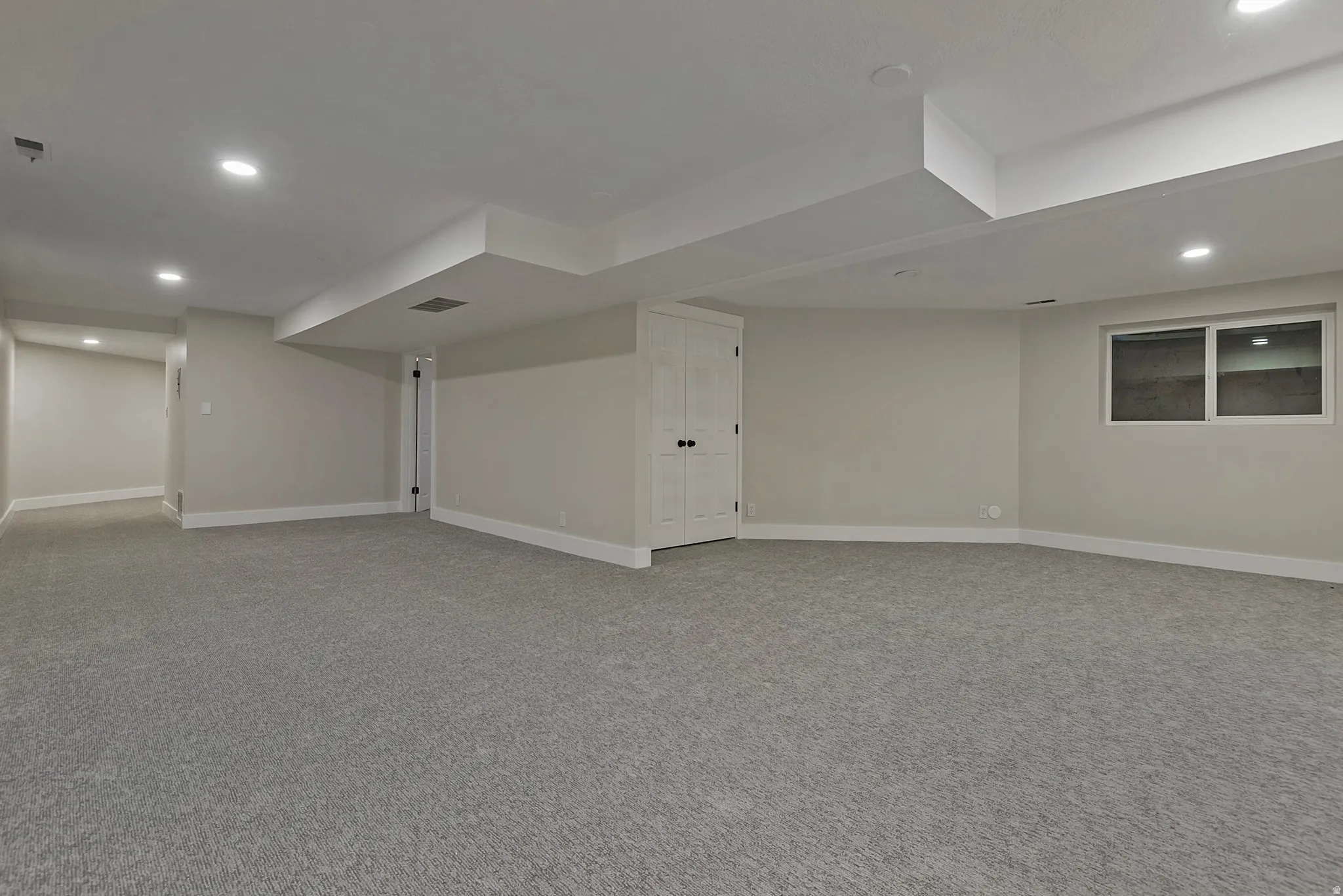 Spacious room featuring gray carpet, recessed lighting, and a white-framed window