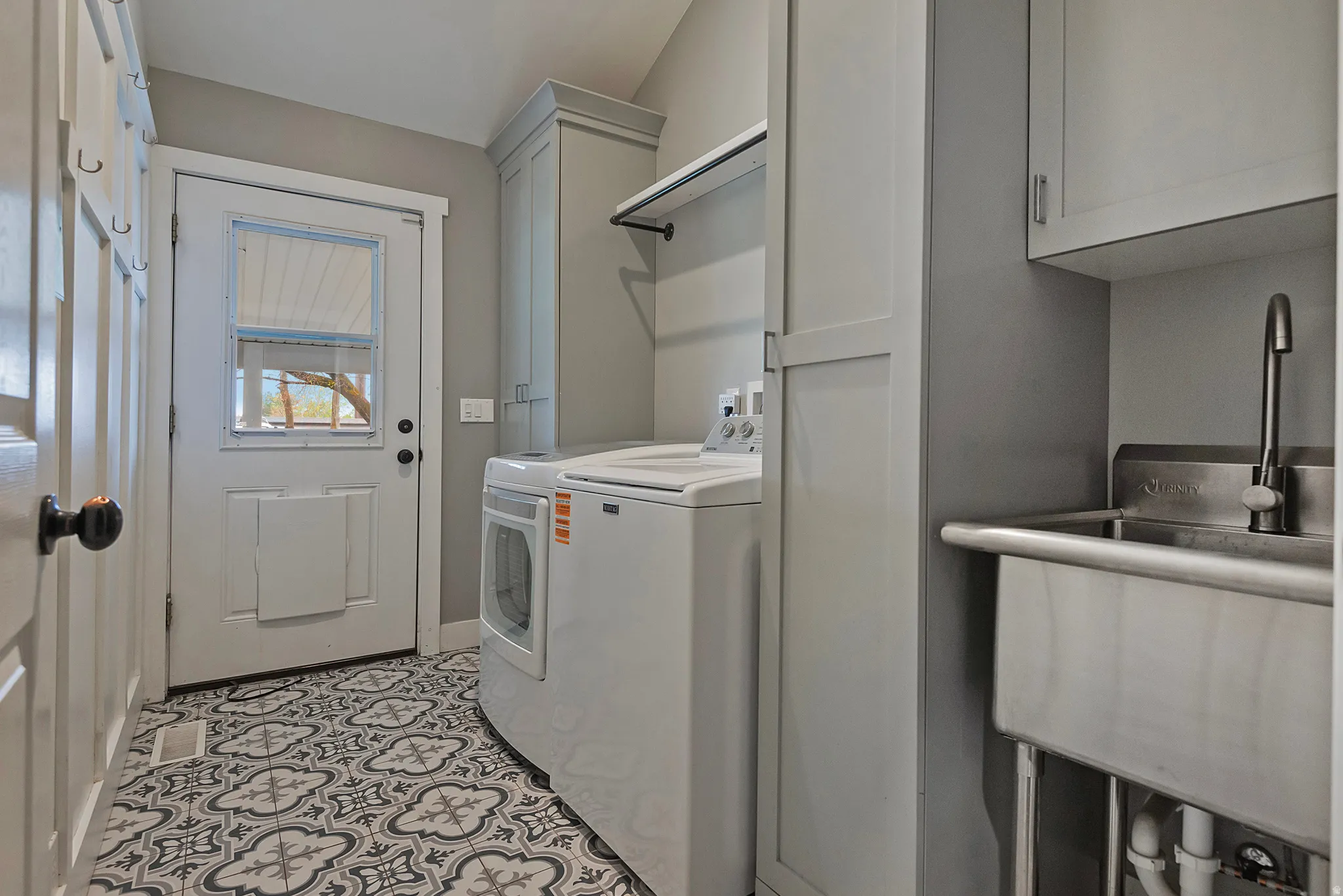 Laundry area featuring patterned tile flooring, built-in cabinetry, a utility sink, and a washer/dryer