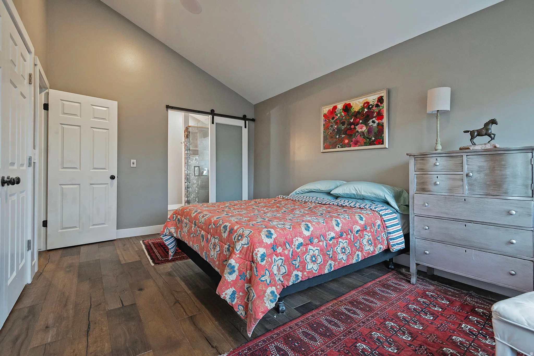 Vaulted ceiling, wood-finish flooring, white paneled doors, and a sliding barn door with frosted glass