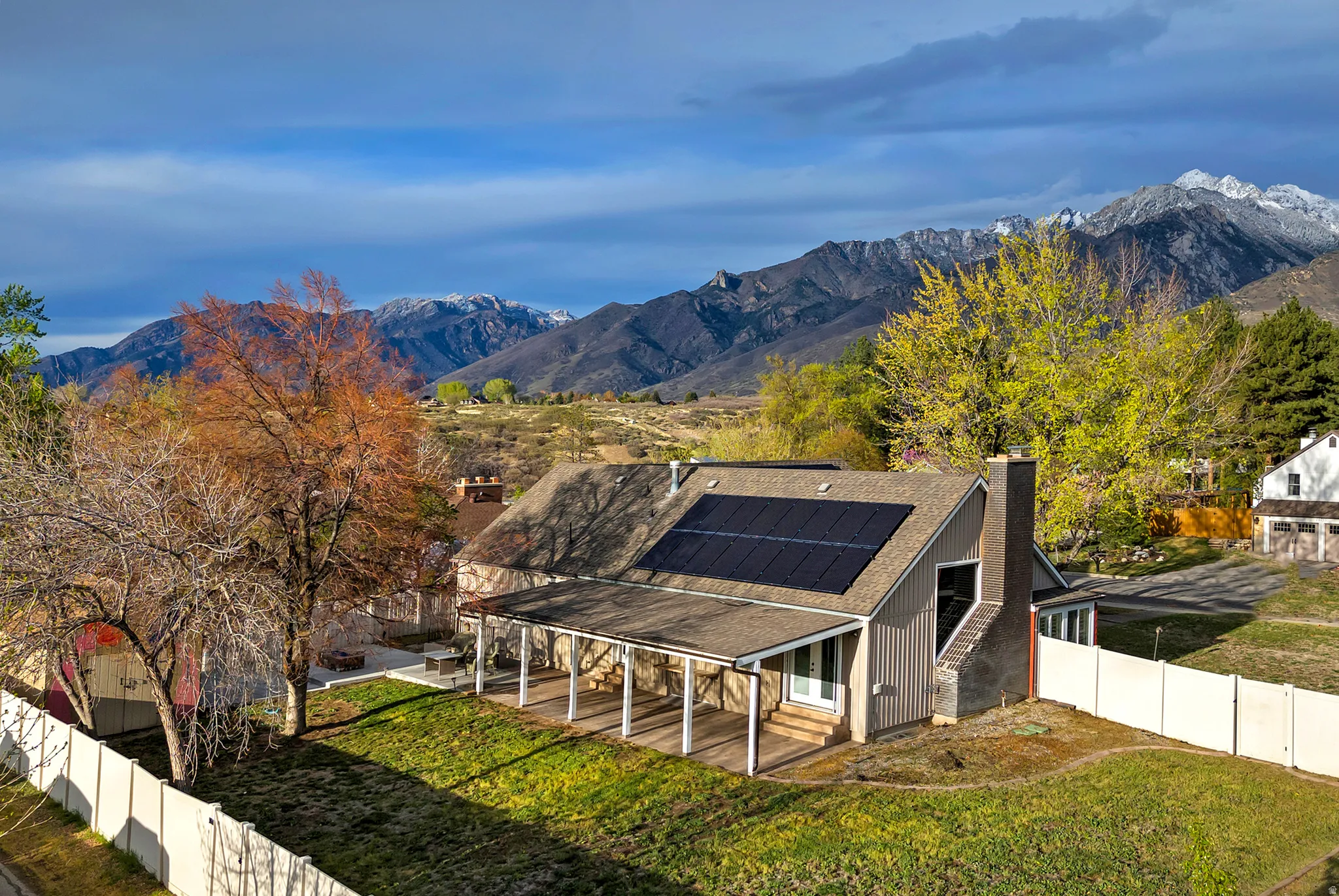 Exterior featuring solar panels, a covered porch with supporting columns, a stone chimney, and a fenced yard