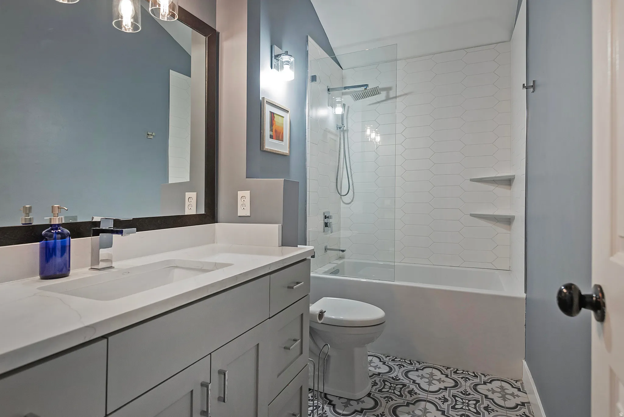 Vanity with integrated sink, rectangular mirror, walk-in shower with glass enclosure, white subway tile surround, and patterned floor tile