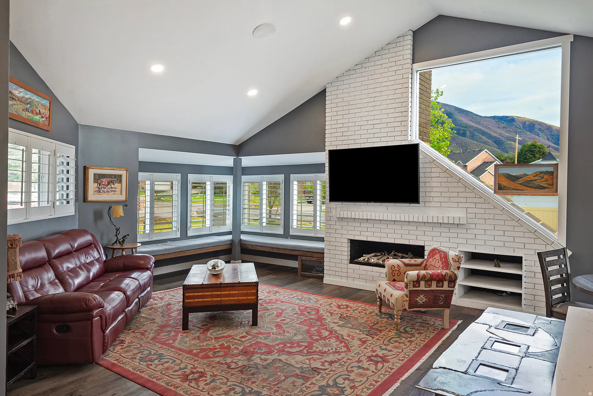 Sophisticated recreation room featuring a corner configuration of multi-pane windows with transom detailing, a linear fireplace with white brick surround and integrated media nook, recessed ceiling lighting, and dark accent wall paneling