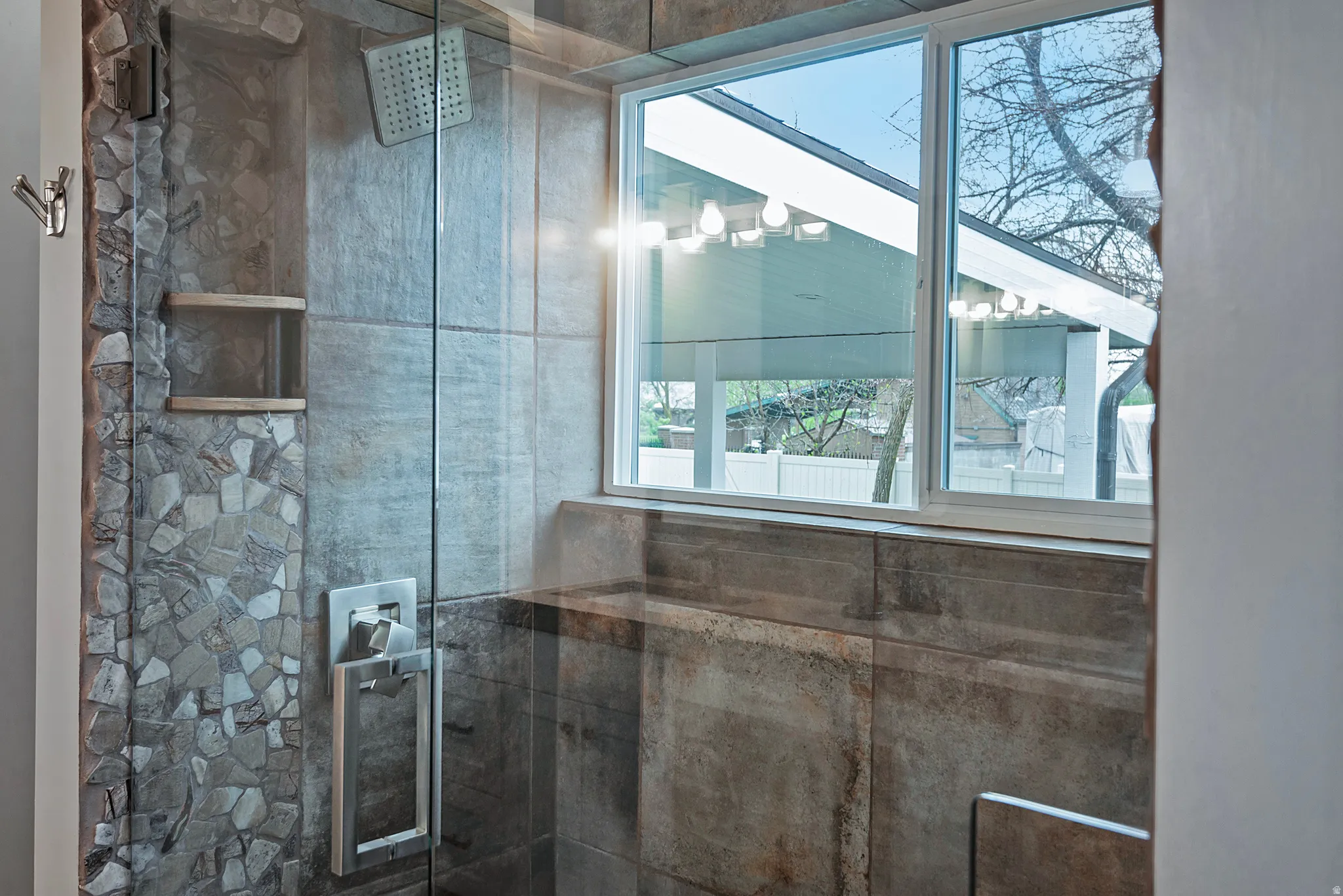 Glass-enclosed shower with a rainfall showerhead, stone tile accent wall, built-in shelving, and a dual-pane window