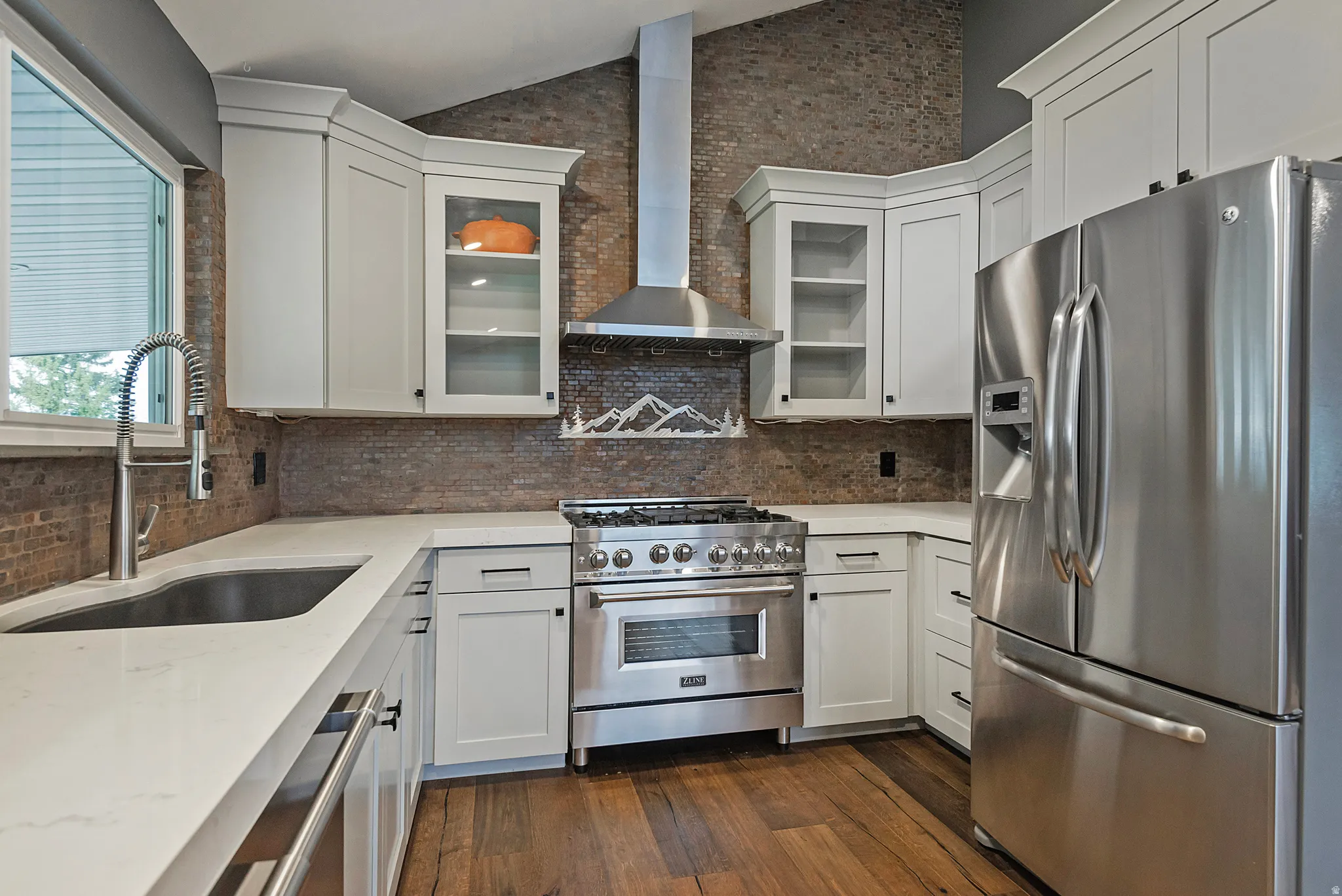 White cabinetry with glass-front accents, stainless steel appliances, solid surface countertops, and a full-height tile backsplash