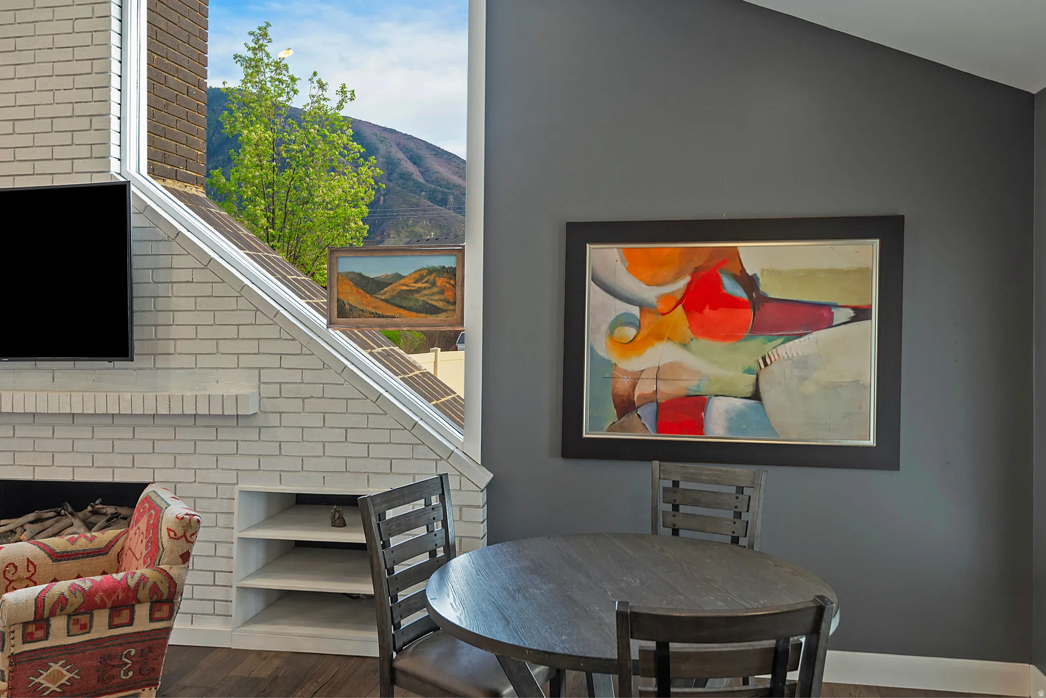 White brick fireplace with built-in shelving, wood-finish flooring, and a large window offering natural light