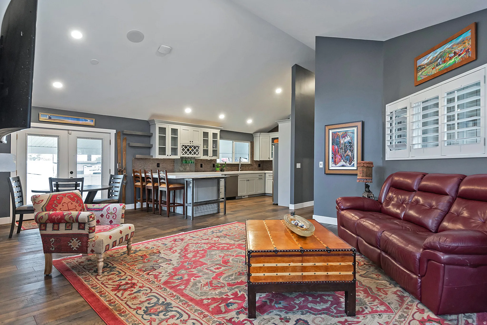 Vaulted ceiling, wood-finish flooring, white cabinetry, kitchen island with counter seating, and glass panel French doors