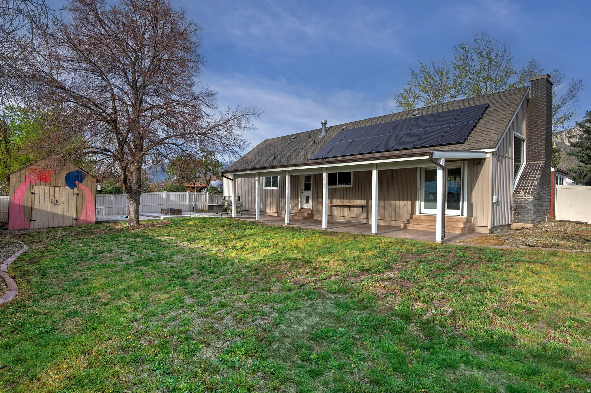 Expansive backyard featuring a covered patio, solar panels, and a storage shed