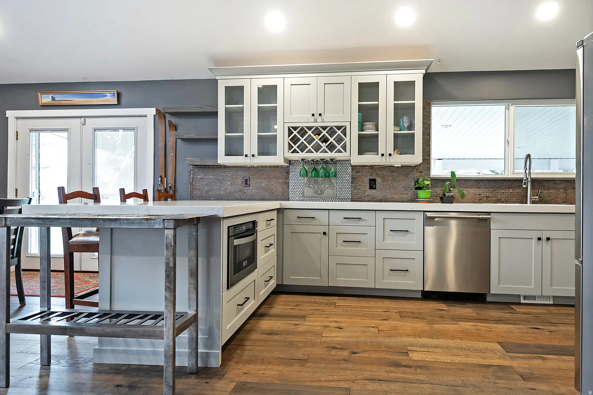 White shaker cabinetry, wood-finish flooring, stainless steel appliances, built-in microwave, and a tile backsplash