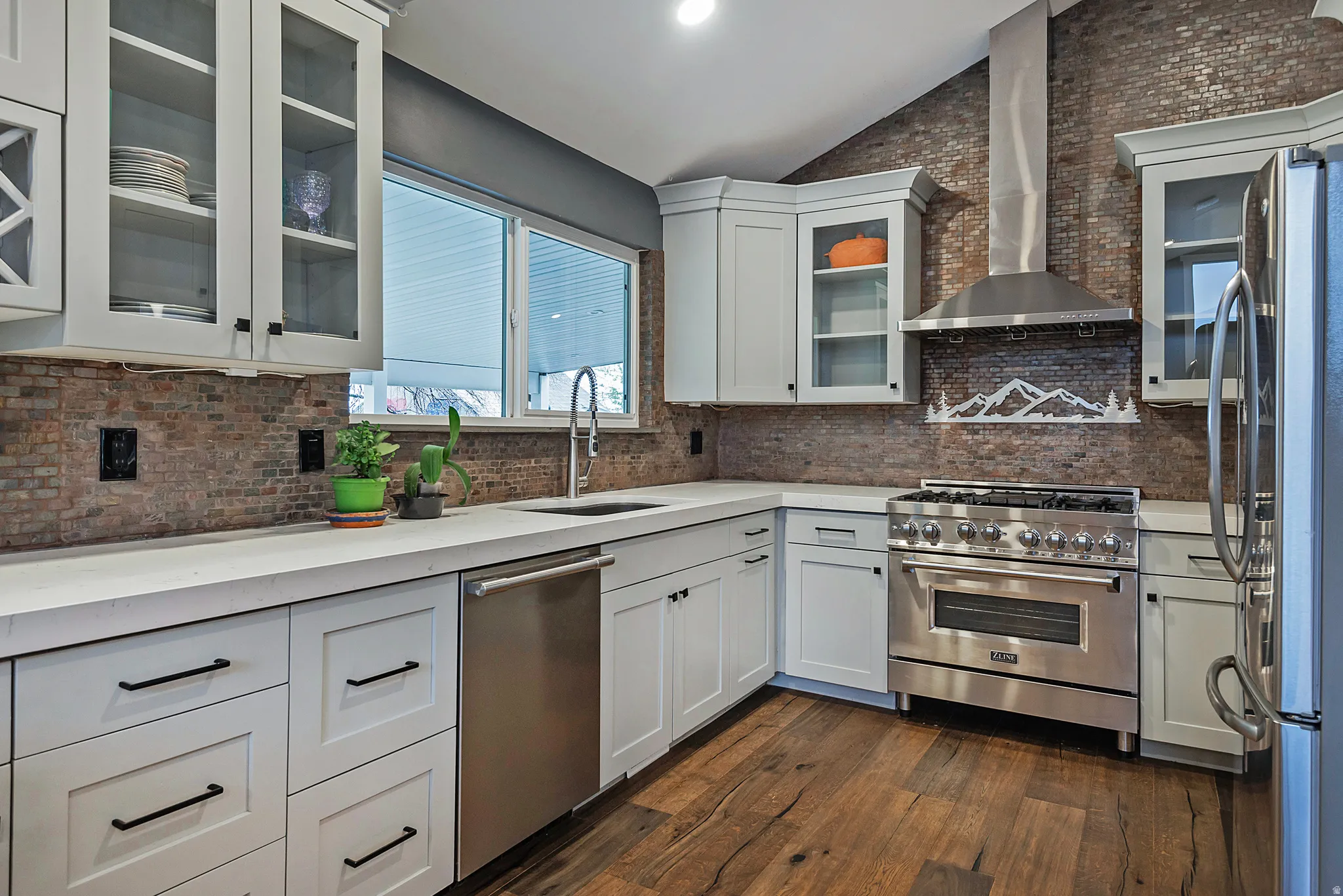 White cabinetry with dark hardware, stone-finish backsplash, stainless steel appliances, wood-finish flooring, and light-toned countertops
