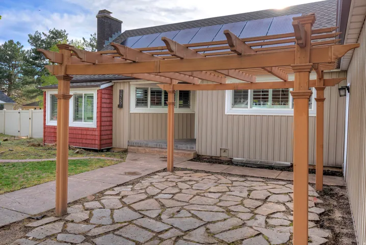 Wood pergola covering a flagstone patio with a concrete walkway