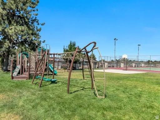 Expansive recreational area featuring a playground structure with slides and climbing elements, a swing set, and a well-maintained basketball court with a chain-link fence