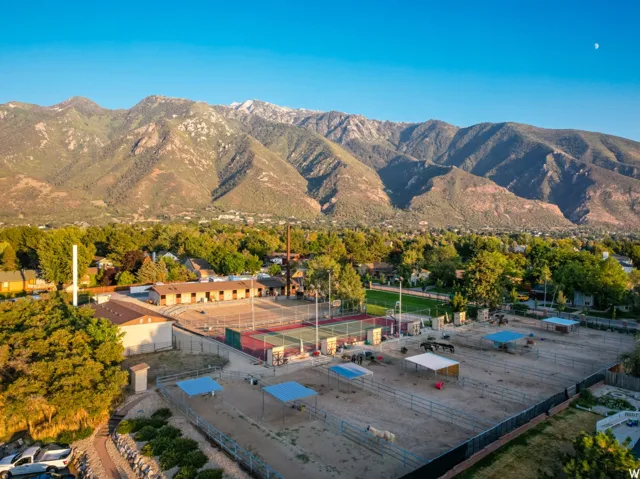 Expansive property featuring multiple animal enclosures with shade structures, two tennis courts, and a large building with multiple entryways, all set against a prominent mountain backdrop