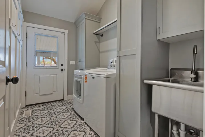 Laundry area featuring patterned tile flooring, built-in cabinetry, a utility sink, and a washer/dryer