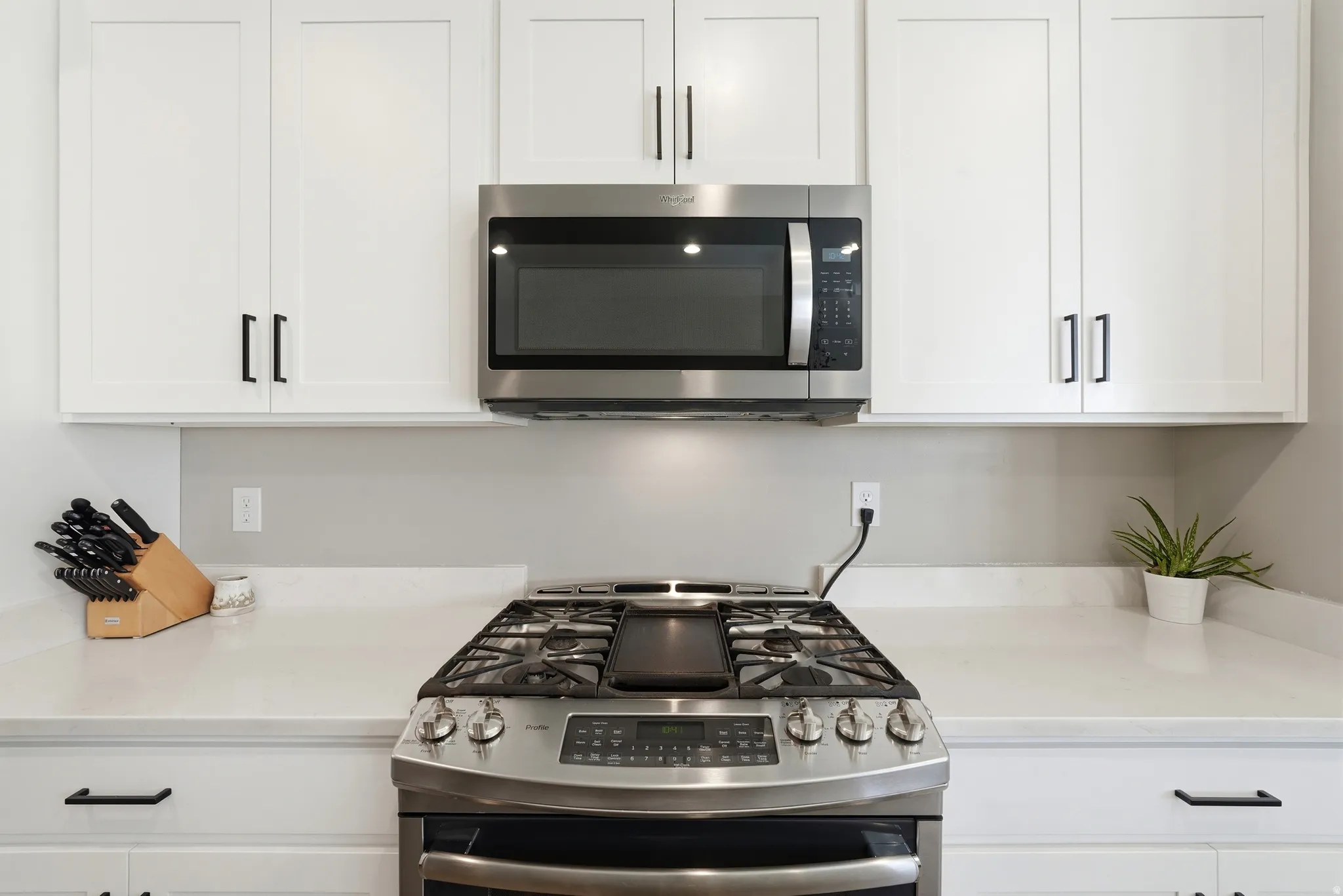 White shaker cabinetry with matte black hardware, stainless steel microwave, stainless steel range, and light-toned countertops