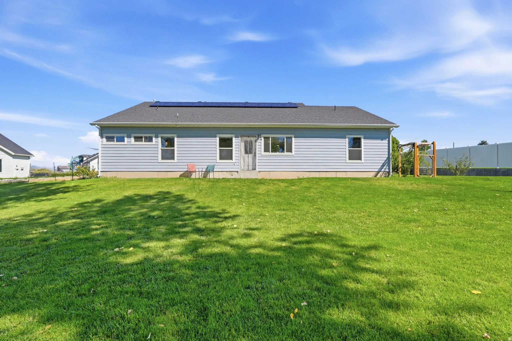 Spacious backyard featuring a manicured lawn, light blue siding, a dark shingled roof, and solar panels