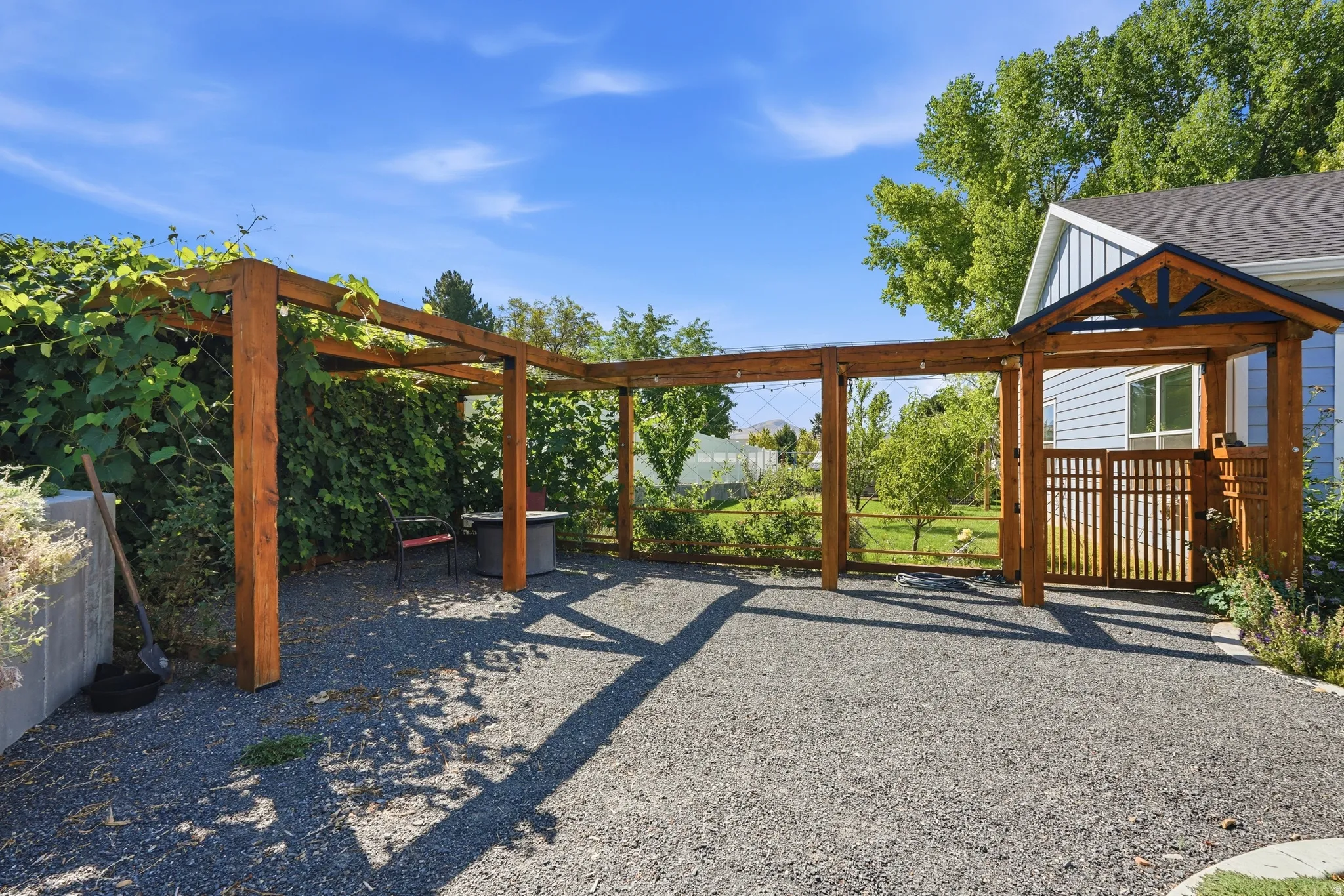 Expansive gravel patio with a wood pergola, integrated wooden gate, and a covered entryway featuring decorative trim