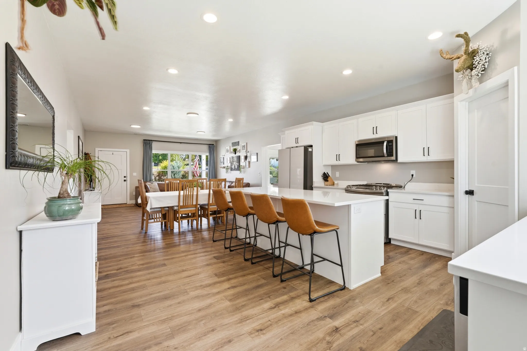 Open-concept living area featuring wood-finish flooring, recessed lighting, white cabinetry, a kitchen island with seating, and stainless steel appliances