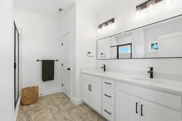 Dual vanity with white cabinetry and integrated sinks, matte black hardware, large frameless mirror, and a walk-in shower with black framing