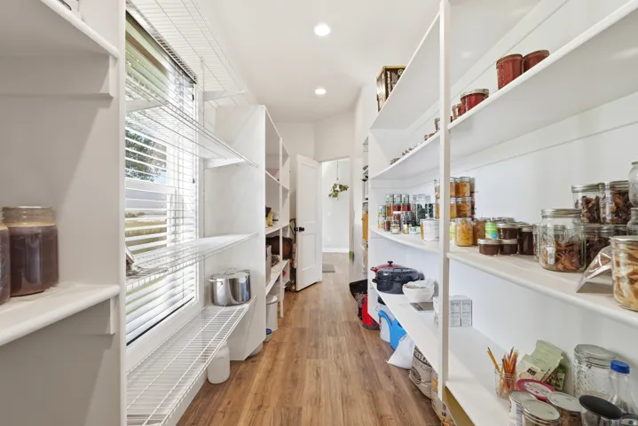 Walk-in pantry featuring extensive built-in shelving, wood-finish flooring, recessed lighting, and a window with blinds