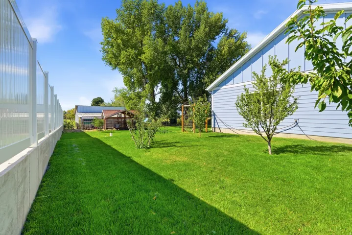 Expansive lawn area bordered by a privacy fence, featuring mature trees and a light blue siding structure