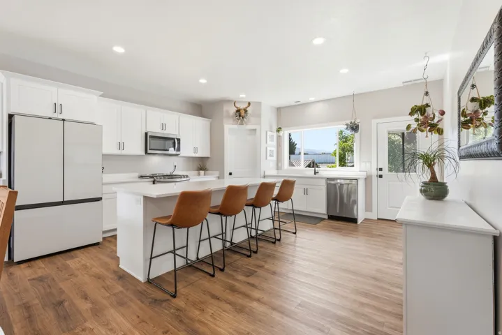 Spacious kitchen featuring white cabinetry, a large center island, stainless steel appliances, wood-finish flooring, and a large window