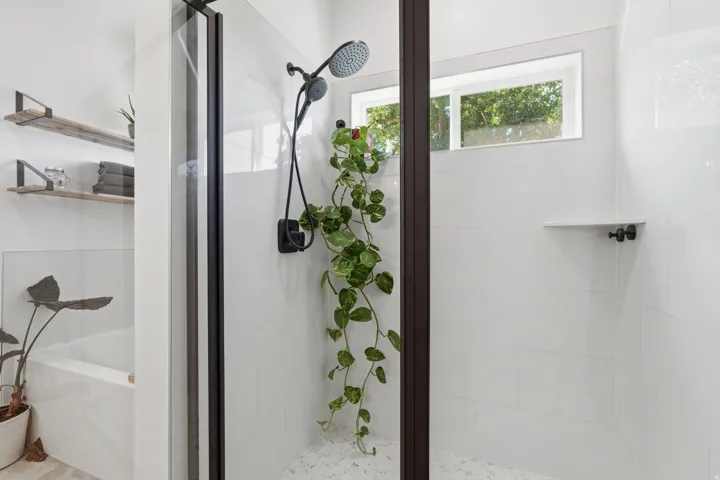 Frameless glass shower enclosure with matte black hardware, white subway tile walls, and a recessed window