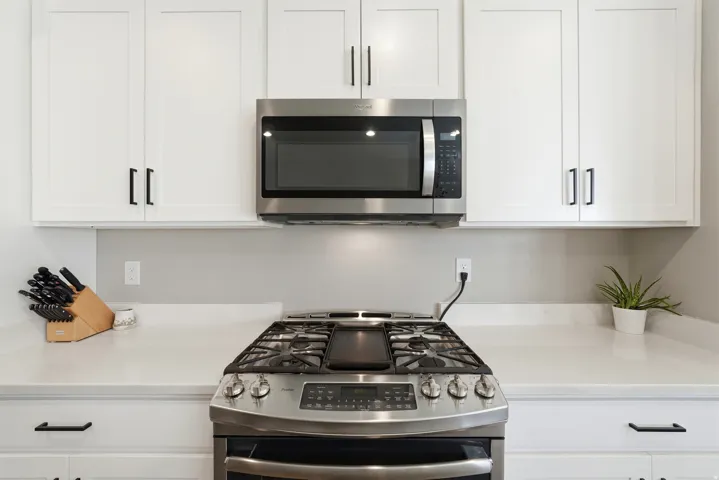 White shaker cabinetry with matte black hardware, stainless steel microwave, stainless steel range, and light-toned countertops
