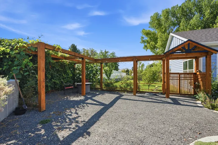 Expansive gravel patio with a wood pergola, integrated wooden gate, and a covered entryway featuring decorative trim