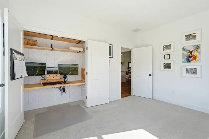 Built-in desk with wood shelving, white walls, and light-colored carpeting